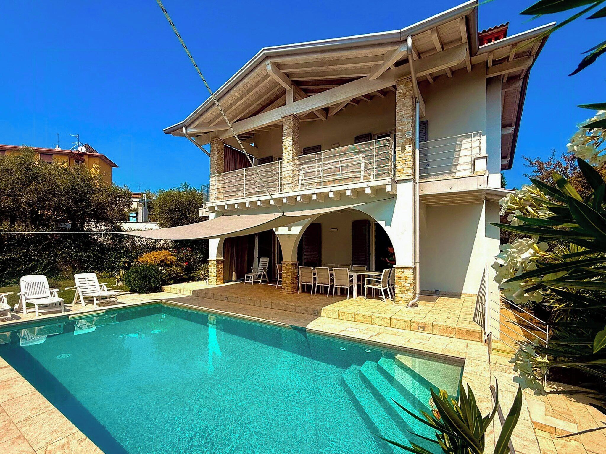 A two-story house with a swimming pool, outdoor seating, and a balcony.
