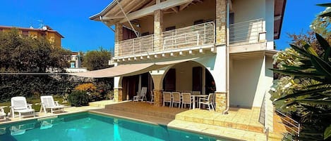 Una casa de dos pisos con piscina, mobiliario exterior y balcón.