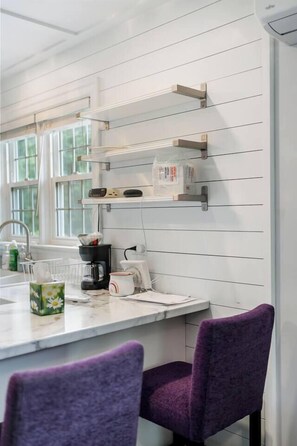 A kitchen with white cabinetry, a coffee maker, and a window with curtains.