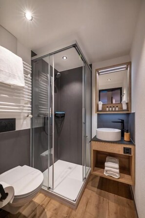Un baño moderno con cabina de ducha de vidrio, un lavamanos blanco y un espejo sobre él.
