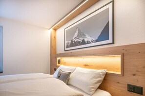 Quarto de hotel com cama, cabeceira com luz embutida e quadro de uma montanha na parede.