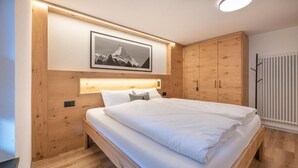 Ein Schlafzimmer mit einem Holzbett, einem an der Bettseite angebrachten Kopfteil mit Beleuchtung, einem gerahmten Bild an der Wand und einem Kleiderschrank.