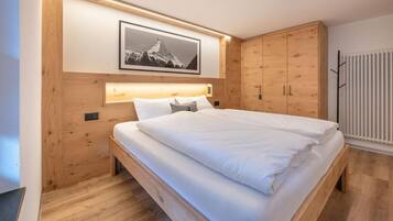 Ein Schlafzimmer mit einem Holzbett, einem an der Bettseite angebrachten Kopfteil mit Beleuchtung, einem gerahmten Bild an der Wand und einem Kleiderschrank.