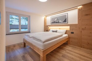 Ein Schlafzimmer mit einem hölzernen Bett, einem Fenster mit Jalousien, einem an der Wand hängenden Bild und einer Wandverkleidung aus Holz.