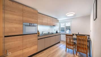Eine moderne Küche mit Holzschränken, einer zentralen Kochinsel und einem Essbereich mit zwei Holzstühlen.