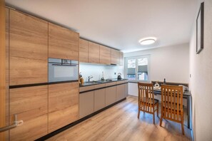 Eine moderne Küche mit Holzschränken, einer zentralen Kochinsel und einem Essbereich mit zwei Holzstühlen.