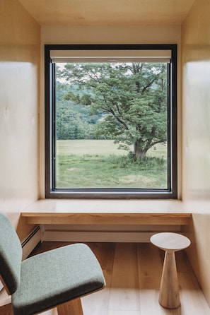 Una habitación con un ventanal grande, un banco de madera y una pequeña mesa redonda.