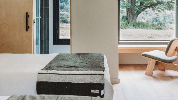 Quarto moderno com cama, um banco e uma janela grande com vista para árvores.