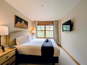 A hotel room with a bed, bedside table, lamp, TV, and a window with curtains. - New Listing | King Bed | Steps from the slopes (Keystone)