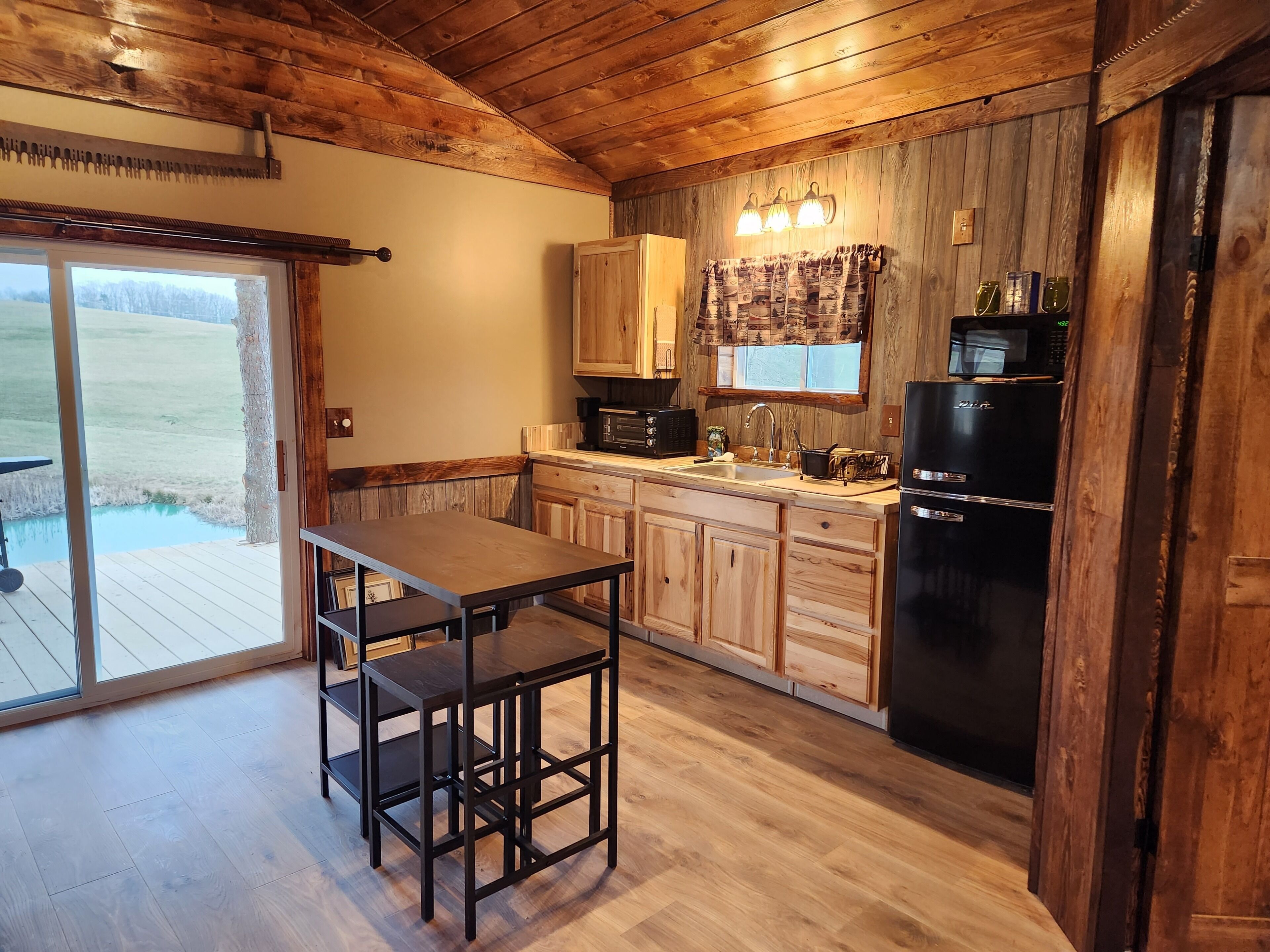 A kitchen with wooden cabinets, a black refrigerator, and a window with curtains.
