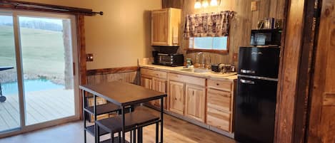 A kitchen with wooden cabinets, a black refrigerator, and a window with curtains.