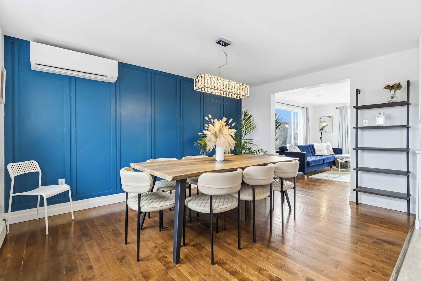 A dining area with a wooden table and chairs, a hanging light fixture, and a blue wall.