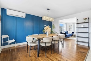 A dining area with a wooden table and chairs, a hanging light fixture, and a blue wall.