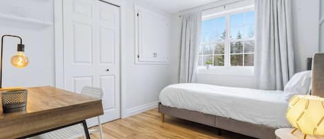 A room with a bed, a desk, a chair, a lamp, and a window with curtains.
