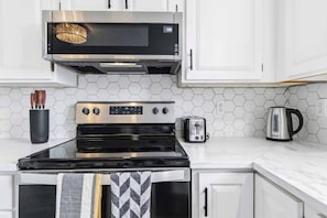 A kitchen with a stainless steel range hood, a black stovetop, a toaster, and a kettle on the counter.