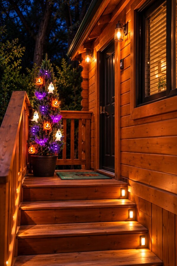 Una cabaña de madera con un porche, un árbol de Navidad con luces y una puerta.