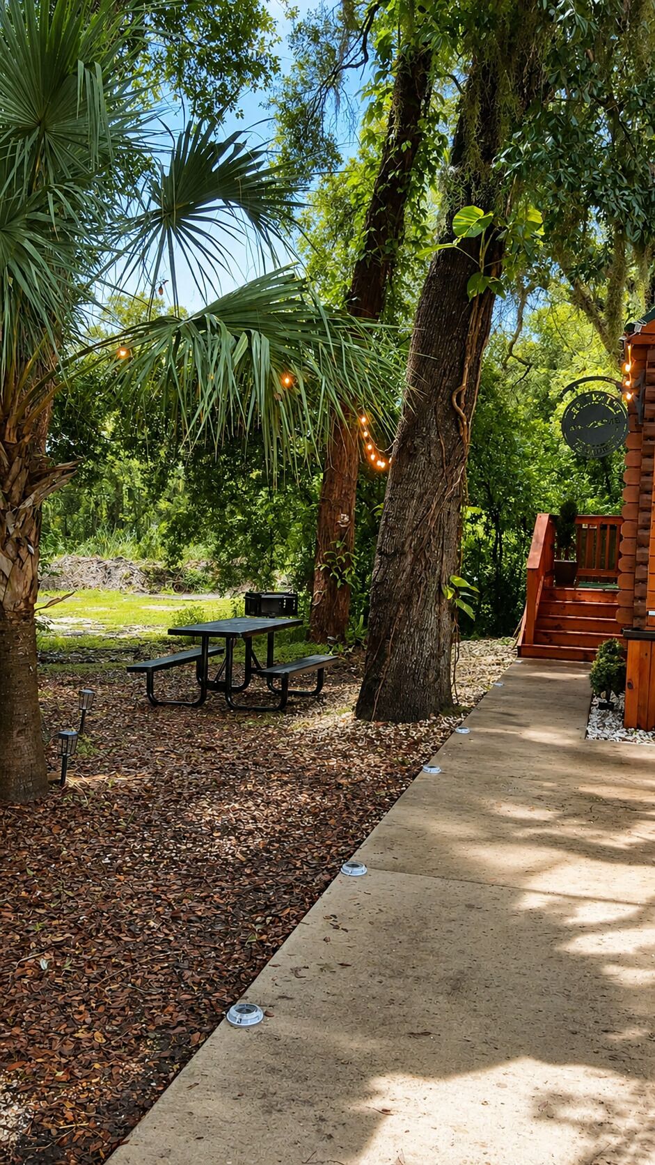 A park area with picnic tables, a concrete path, and trees.