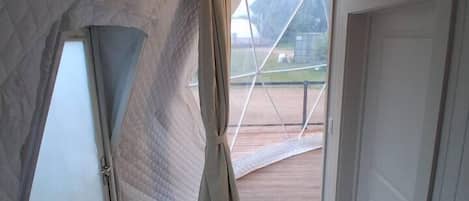 Un pasillo estrecho con suelo de madera, paredes blancas y vista a un campo deportivo a través de un ventanal.