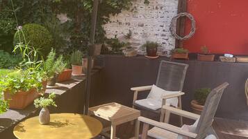 Una terrazza esterna con un tavolo rotondo, due sedie, un ombrellone grande e diverse piante in vaso.