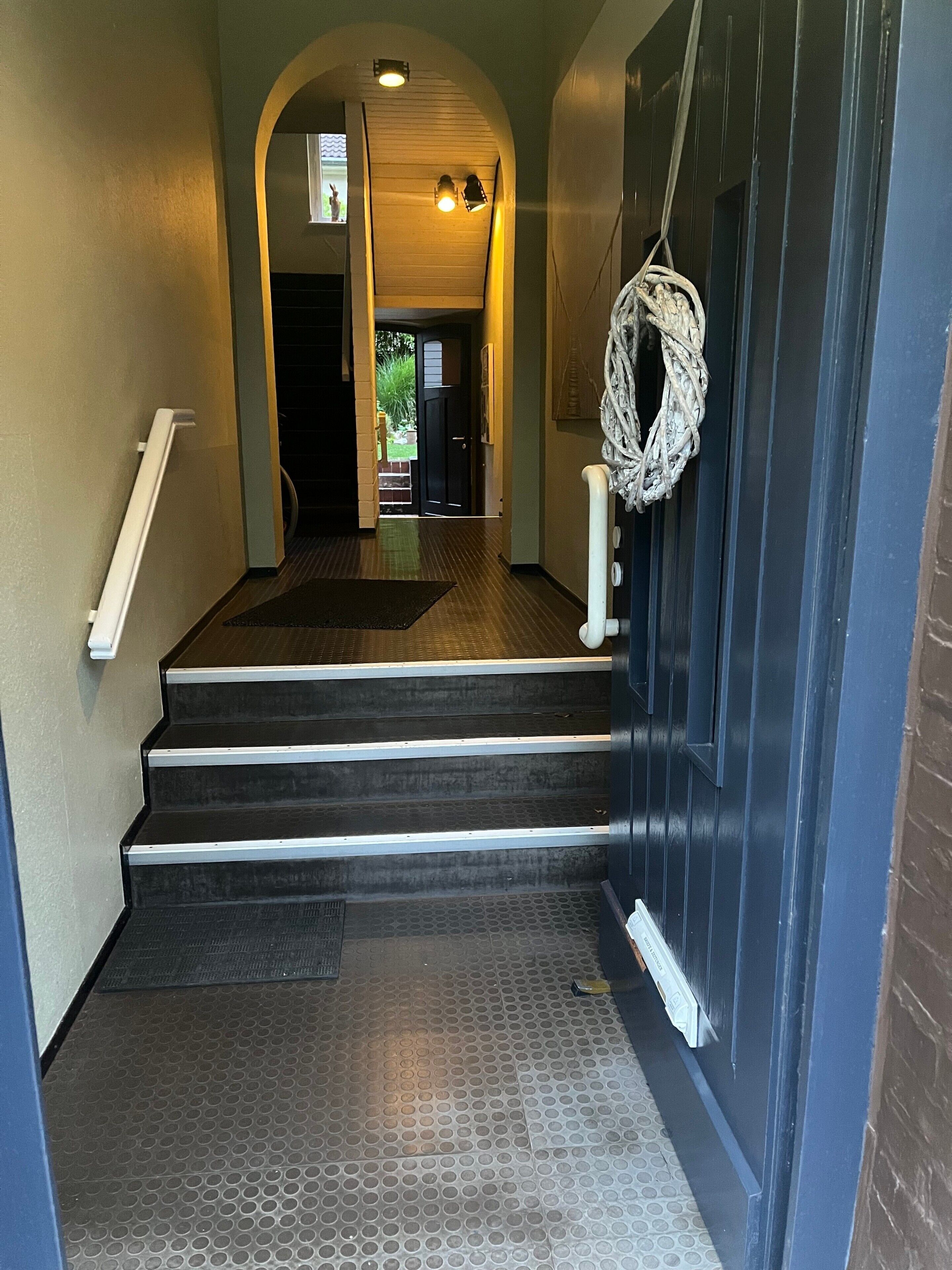 Eine Treppe führt zu einer Tür, vor der sich eine strukturierte Fußmatte befindet.