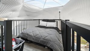 Un dormitorio moderno con un diseño geométrico en el techo, una cama con colcha gris y una pequeña mesa con una silla.