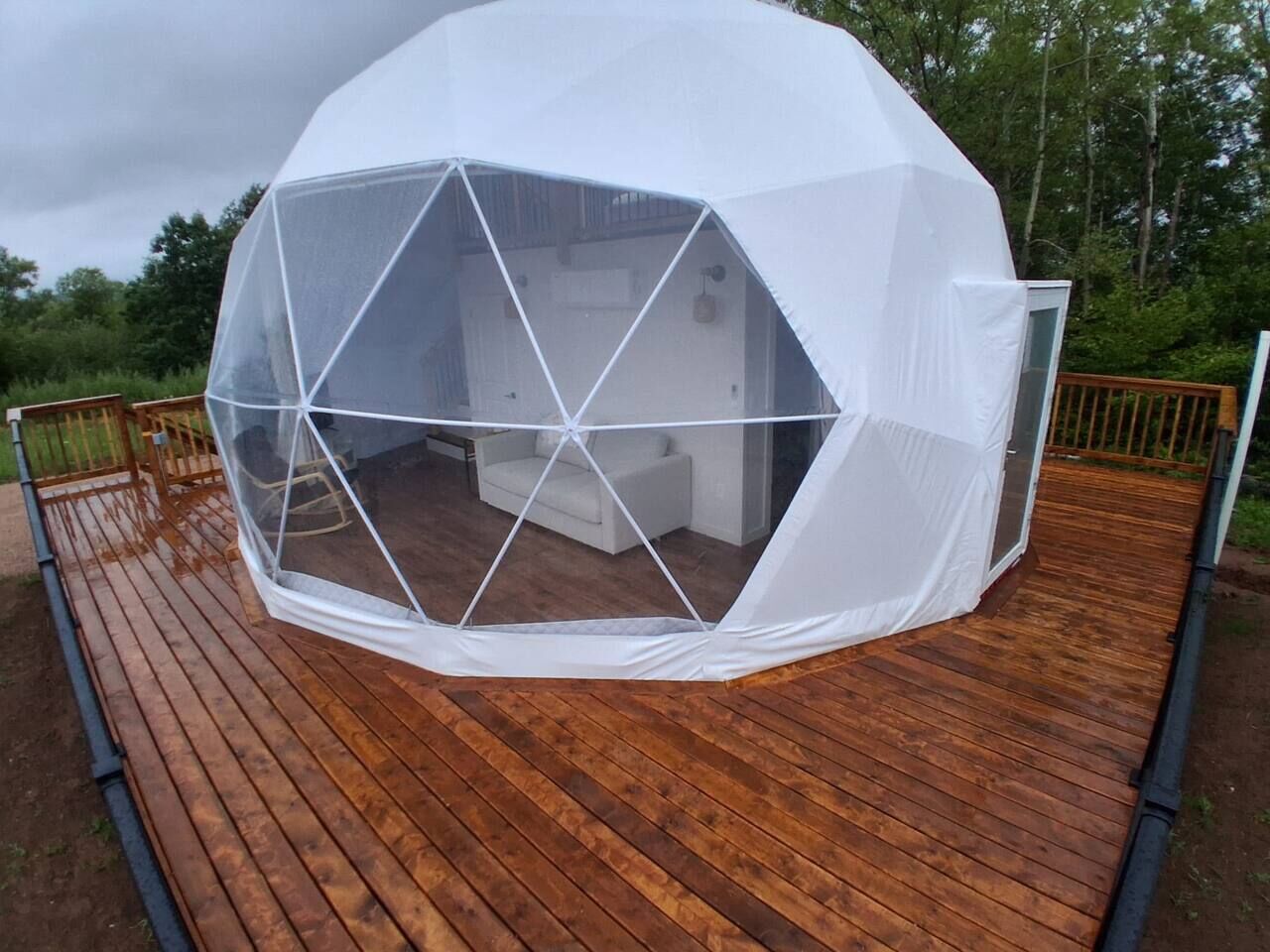 A geodesic dome structure with a transparent roof, situated on a wooden deck.