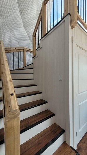 Un escalier avec des marches en bois et des rampes noires, menant à une porte blanche.