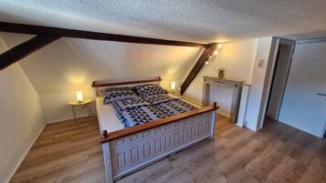 A bedroom with a sloped ceiling, a bed with a patterned bedspread, a bedside lamp, and a small table with a lamp.