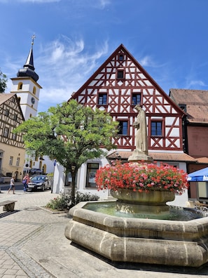 Ein traditionelles Fachwerkhäuschen mit einem Uhrturm, einer Blumenfontäne und einem gepflasterten Platz.
