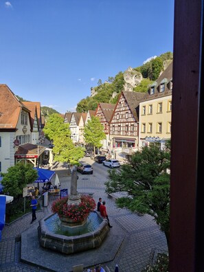 Ein stimmungsvoller Stadtplatz mit traditioneller Architektur, einem Brunnen und blauem Himmel.