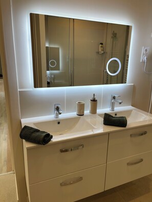 A bathroom with a white vanity, a mirror, a sink, and a towel.
