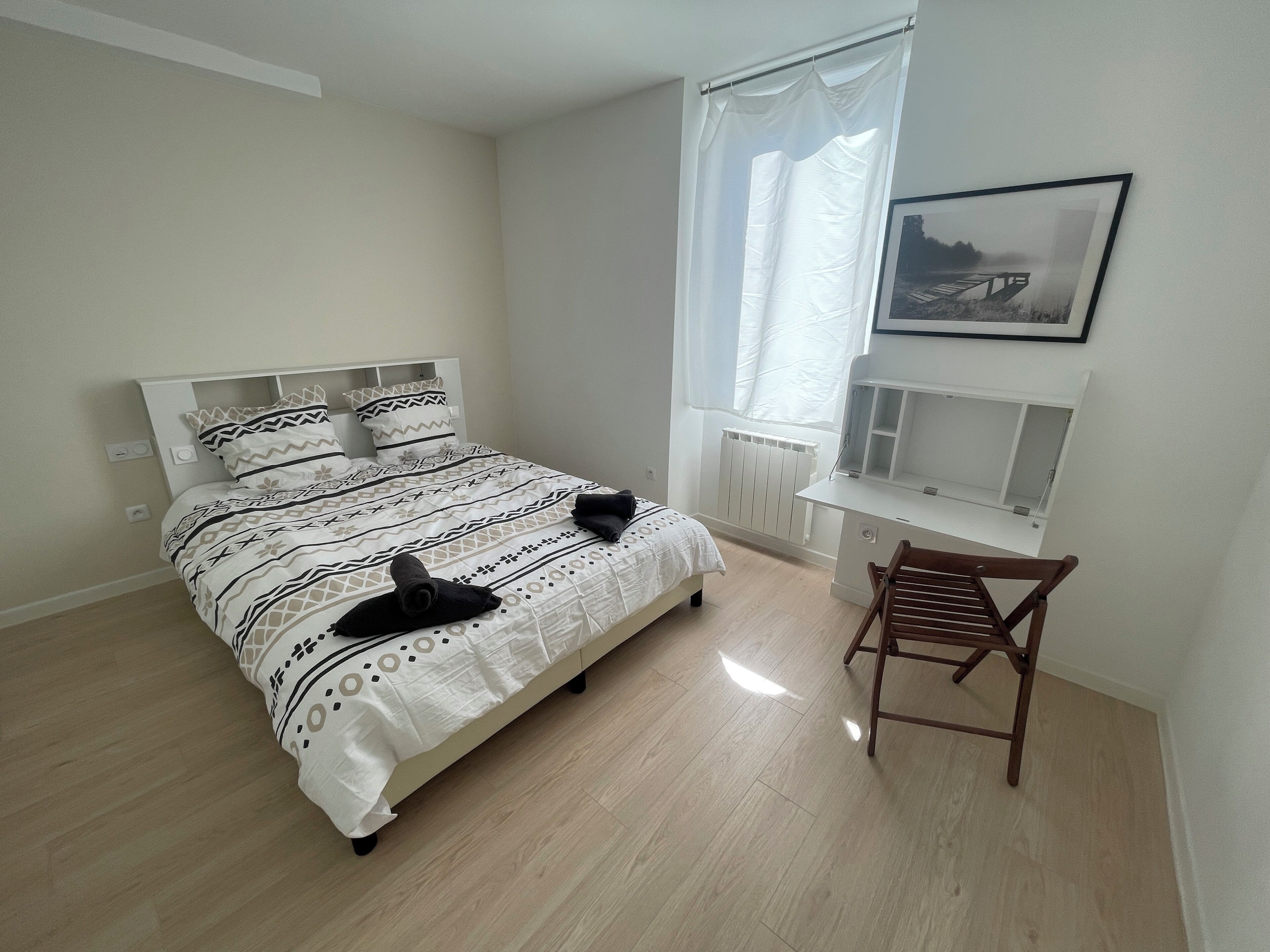 A bedroom with a bed, a chair, a window with curtains, a radiator, and a picture on the wall.