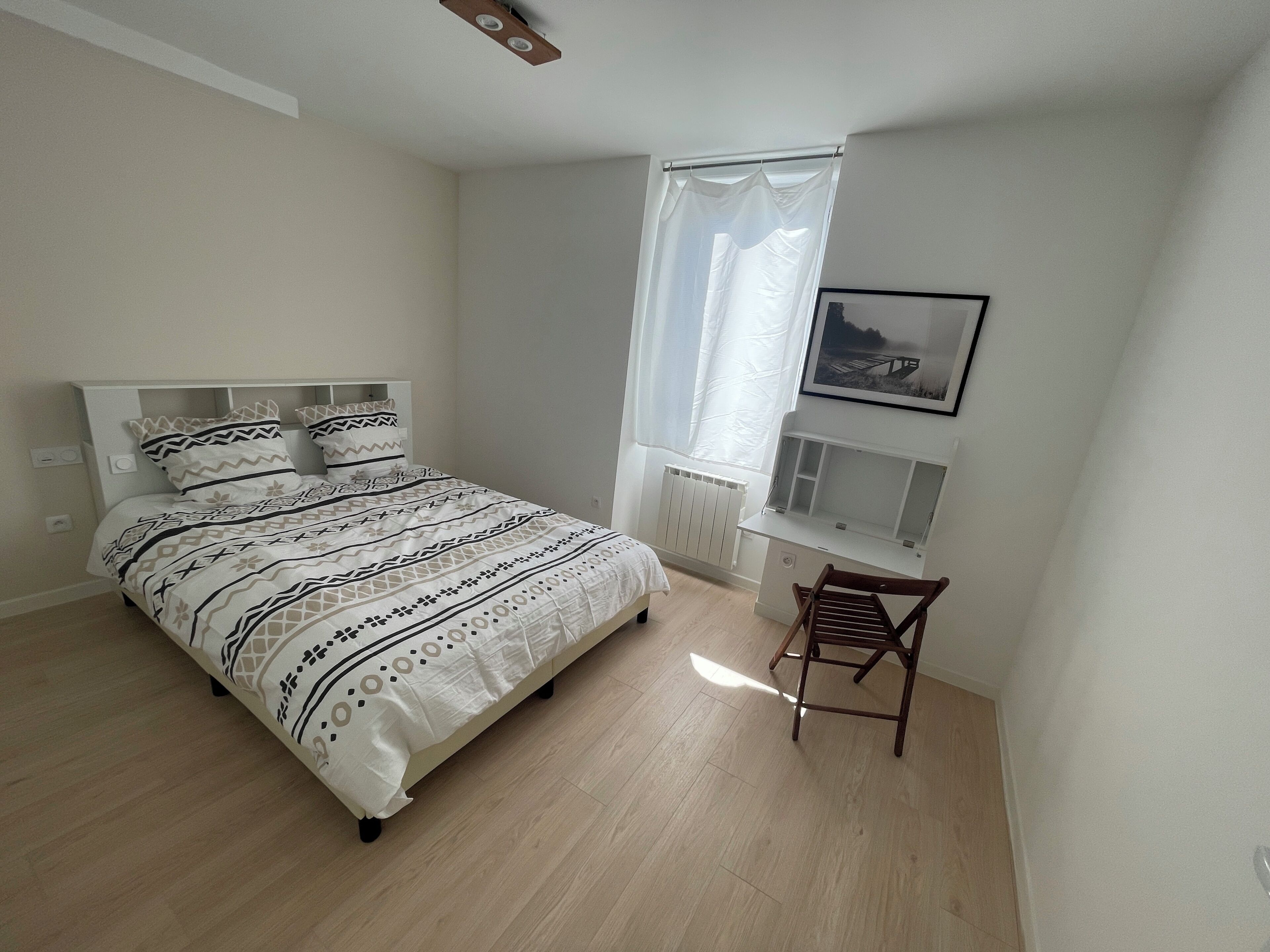 A bedroom with a bed, a chair, a radiator, and a window with a curtain.