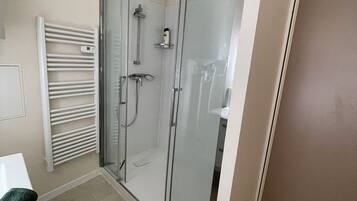 A bathroom with a glass shower enclosure, a white radiator, and a green towel on a white surface.