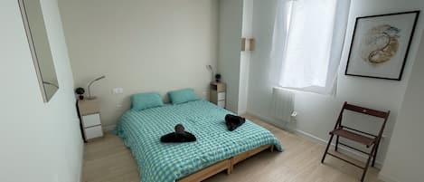 A bedroom with a bed, bedside tables, a chair, a window with curtains, and a wall-mounted artwork.