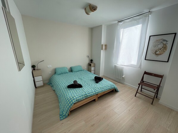 A bedroom with a bed, bedside tables, a chair, a window with curtains, and a wall-mounted artwork.