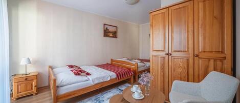 A room with a bed, a small table with cups, a chair, and a wardrobe.