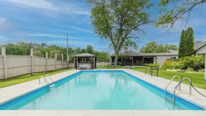 Uma piscina retangular com uma banheira de hidromassagem e uma área de estar coberta em um quintal.