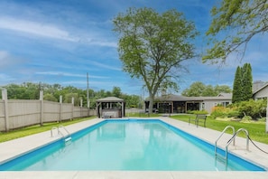 Ein rechteckiger Pool mit Whirlpool und überdachtem Sitzbereich in einem Garten.