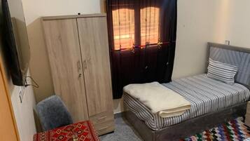 A bedroom with a bed, a wardrobe, a television, and a small table with a patterned tablecloth.