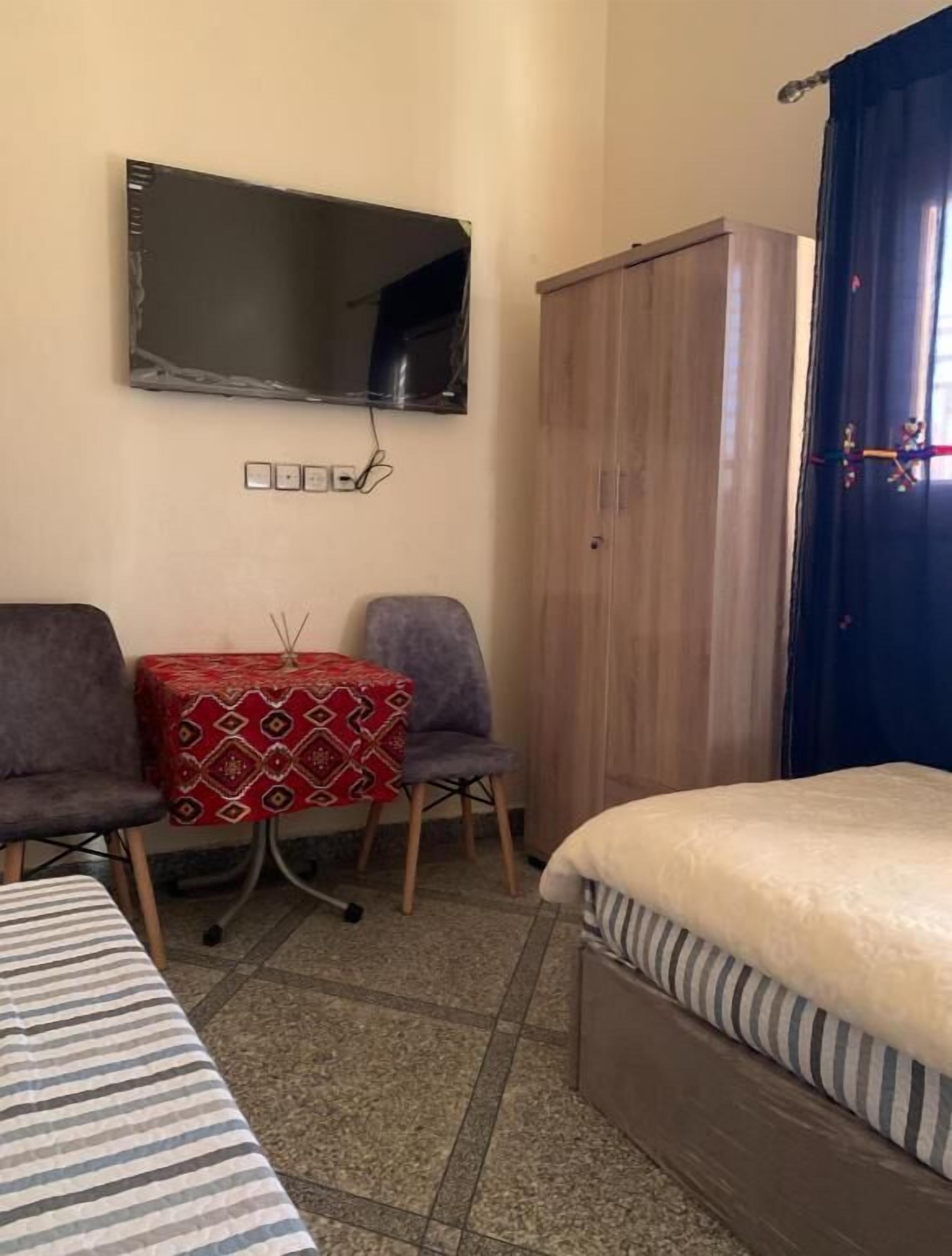 A hotel room with a bed, a small table with chairs, a wardrobe, and a television mounted on the wall.