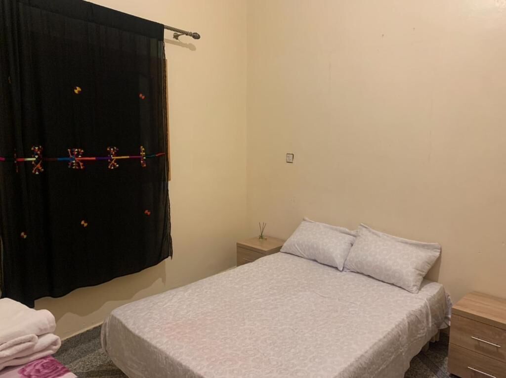 A bedroom with a bed, a nightstand, a drawer, and a curtain.