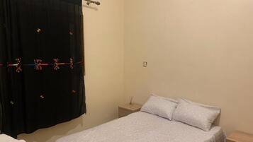 A bedroom with a bed, a nightstand, a drawer, and a curtain.