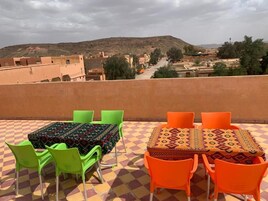Una terraza con piso a cuadros, una mesa con sillas y vista a un pueblo y colinas a lo lejos.
