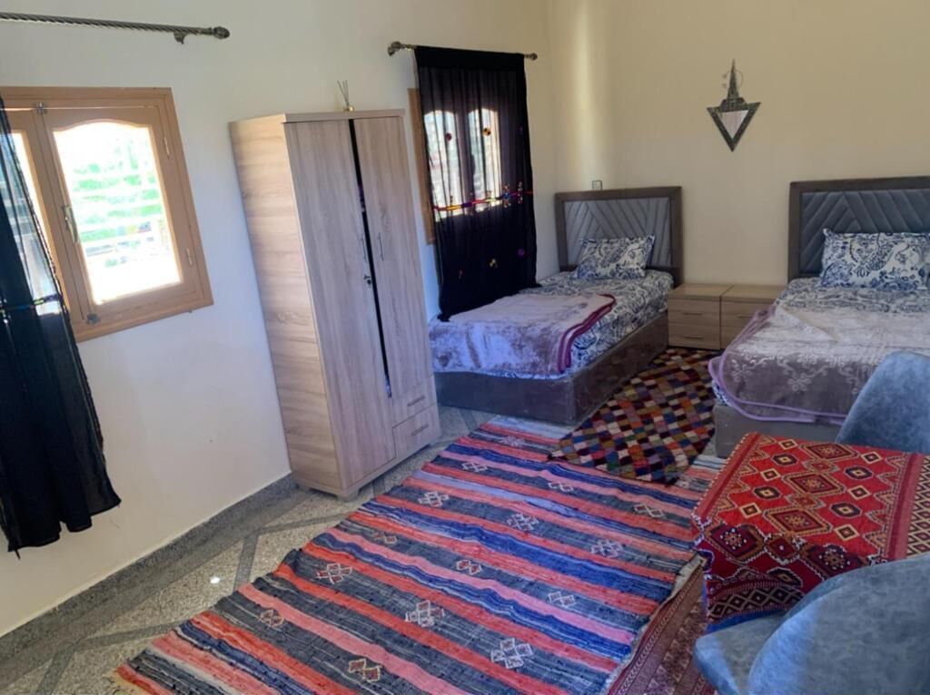 A bedroom with two beds, a wardrobe, a window with curtains, and a patterned rug.
