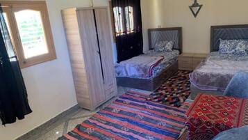 A bedroom with two beds, a wardrobe, a window with curtains, and a patterned rug.