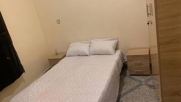 Ein Schlafzimmer mit einem Bett, einem Nachttisch, einem Holzschrank und einem Fliesenboden.