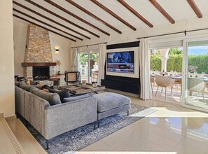 En moderne stue med en stenspir og et stort fladskærms-tv, en grå modulsofa og en balkon med udendørs møbler.