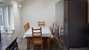 Een kleine keuken met een eettafel, stoelen, een koelkast en een raam.
