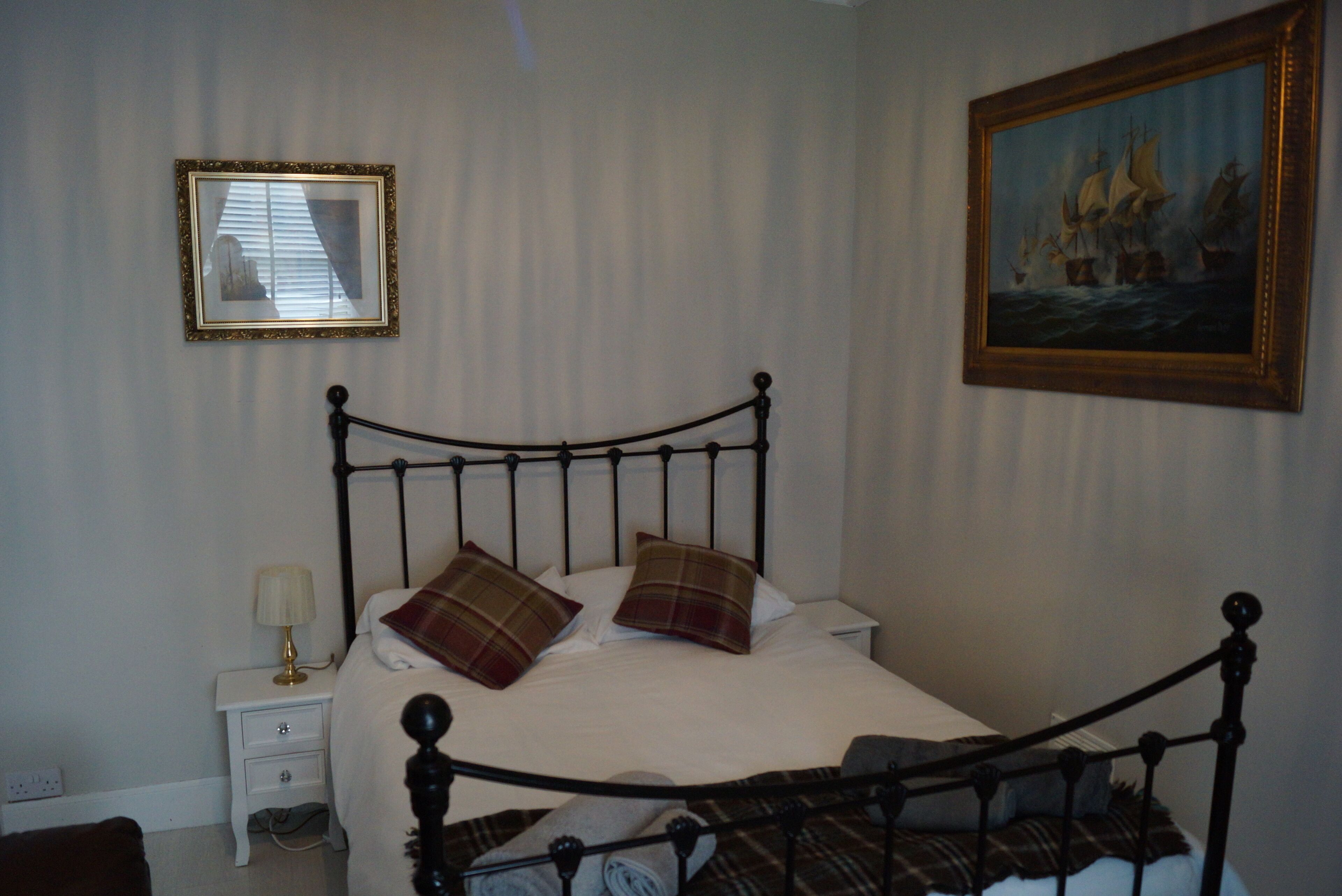 A bedroom with a bed, a nightstand, a lamp, and two framed pictures on the wall.